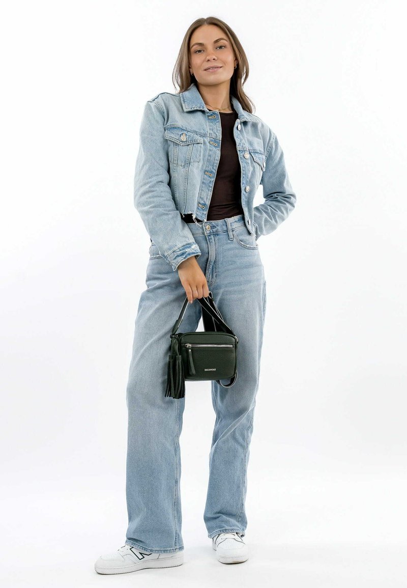 Giacca di jeans di colore azzurro chiaro, abbinata a jeans chiari a vita alta, sneakers bianche e una piccola borsa in pelle nera con frange.