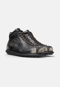 Black leather boots with a distressed gray toe cap, rounded shape, and black rubber sole. Features metal eyelets and laces for closure.