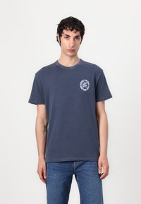 Marineblå bomull T-skjorte med rund hals, korte ermer og et frontgrafikk i hvitt og rødt med et sirkulært design.
