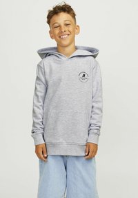 Hanorac gri deschis cu un buzunar tip kangaroo, manșete cu coaste și un logo rotund pe piept. Purtați cu pantaloni scurți largi de un bleu deschis.