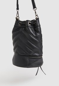 Borsa a secchiello in pelle nera con motivo a zig-zag trapuntato, parte superiore con coulisse e fondo con cerniera. Presenta dettagli in metallo e una tracolla removibile.