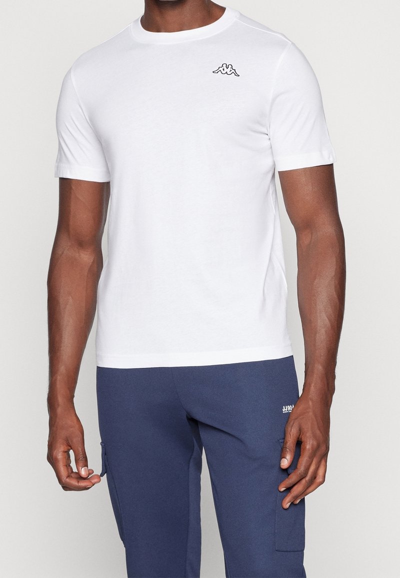 Bílý bavlněný tričko s krátkým rukávem a kulatým výstřihem. Na levé straně hrudi se nachází černé logo Kappa. Hladká textilie.