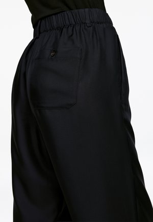 Schwarze, weiche Stoffhosen mit elastischem Bund, seitlichen Taschen und einer einzigen geknöpften Gesäßtasche. Maßgeschneidert für einen lässigen Sitz.