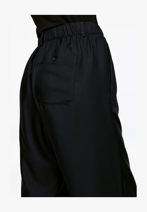 Black, soft fabric trousers featuring an elastic waistband, side pockets, and a single buttoned back pocket. Tailored for a relaxed fit.