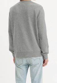 Sudadera gris con mangas largas y cuello redondo. Textura suave, corte relajado y puños acanalados. Combinada con unos vaqueros de denim en azul claro.