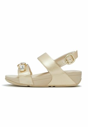 Sandalia de cuña beige con punta abierta y dos correas, una de ellas con una gran piedra decorativa transparente y una correa ajustable con hebilla en el talón.