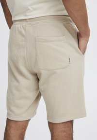 Bermudas de algodón beige con cintura elástica y un bolsillo trasero. La tela es suave con una ligera textura. Diseño simple y limpio.
