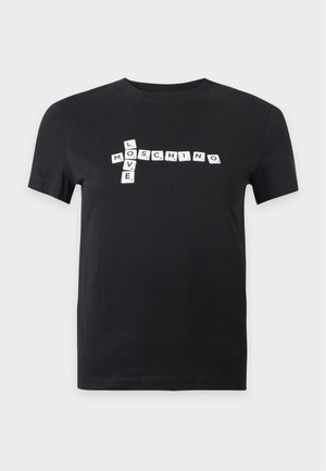 Femme portant un t-shirt noir avec des blocs de lettres blanches épelant "LOVE MOSCHINO" et un jean bleu à jambes larges, debout devant un fond blanc uni.