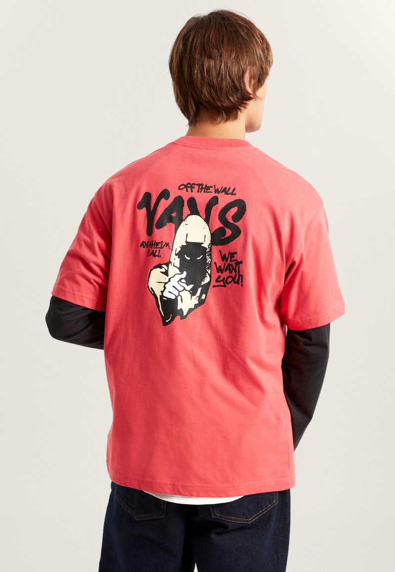 T-shirt graphique couleur corail, avec une impression noire d'une figure encapuchonnée et du texte au dos. Manches courtes, coupe décontractée, en tissu de coton.