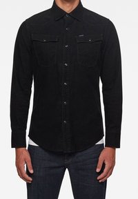 Czarna koszula z korduroy'owych materiałów z długimi rękawami, z przodem zapinanym na guziki, dwiema kieszeniami na piersi oraz przeszytymi szwami na ramionach. Subtelna faktura i klasyczny krój.