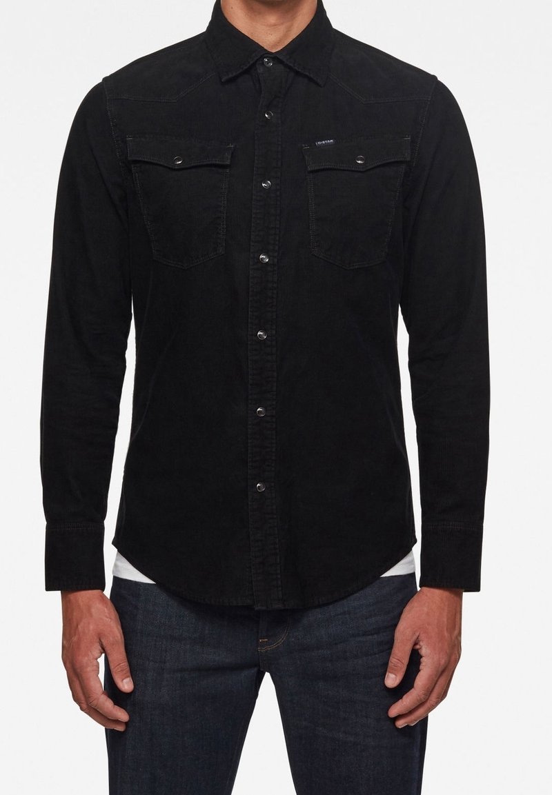 Czarna koszula z korduroy'owych materiałów z długimi rękawami, z przodem zapinanym na guziki, dwiema kieszeniami na piersi oraz przeszytymi szwami na ramionach. Subtelna faktura i klasyczny krój.