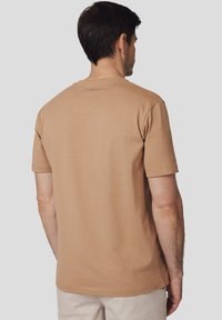 Beżowa bawełniana koszulka z krótkim rękawem, okrągłym dekoltem i prostym wykończeniem. Posiada minimalne przeszycia na ramionach.