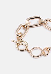 Bracciale a catena color oro caratterizzato da anelli ovali e circolari, con chiusura a toggle e texture liscia e lucida.