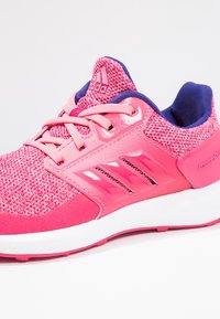 Světlé růžové běžecké boty Adidas s pleteným svrškem, polstrovanou bílou podrážkou, růžovými tkaničkami a modrým polstrovaným límcem.