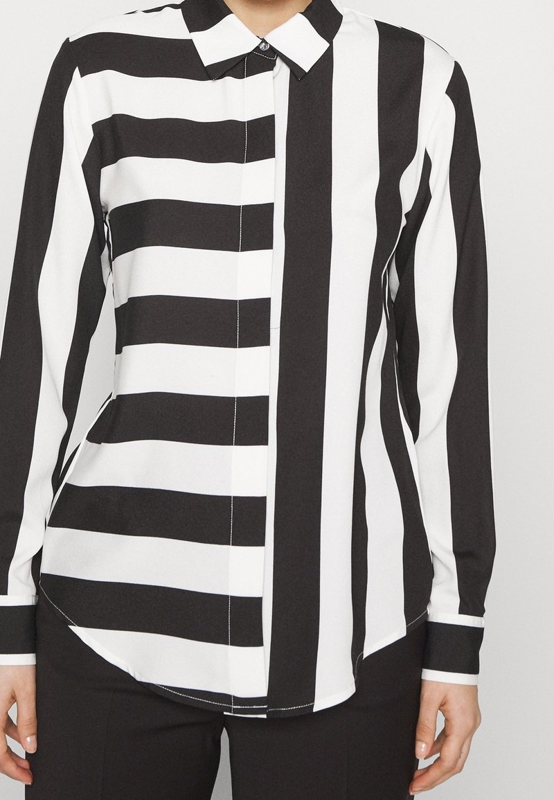 Femme portant une chemise boutonnée rayée noire et blanche avec des rayures horizontales sur le côté gauche et des rayures verticales sur le côté droit.
