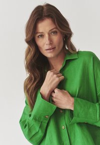 Green linen shirt with long sleeves, button closure, and a collar. The fabric has a slight texture, and the buttons are pale brown.