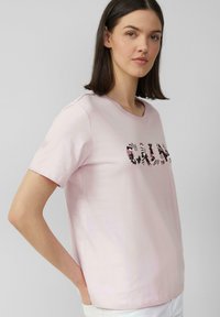 T-shirt rose clair à manches courtes et col rond, présentant un design de texte avec un motif floral sur le devant.
