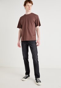 Brown cotton t-shirt with a crew neck and short sleeves, paired with dark denim jeans and black sneakers featuring white soles.