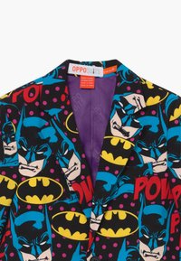 Zwarte blazer met Batman en grafische elementen in stripstijl in levendige kleuren. Binnenkant gevoerd in paars met zichtbaar "OPPOSUITS" label.