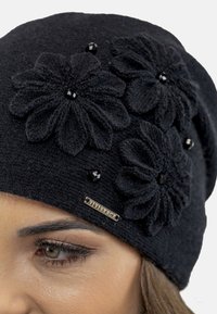 Black knitted beanie featuring three textured flower appliqués with black bead centers and a small metallic label on the side.