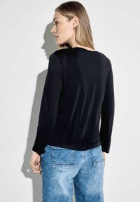 Svart långärmad topp med rund hals, tillverkad av ett mjukt material. Kombinerad med ljusblå denimjeans med bakfickor och blekt textur.