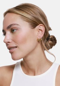 Boucles d'oreilles dorées avec trois anneaux décal�és ornés de petites pierres claires, présentées sur un modèle aux cheveux châtain clair.