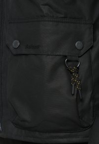 Μαύρο μπουφάν από λείο ύφασμα με τσέπη με καπάκι και κούμπωμα με κουμπί. Διαθέτει διακοσμητικό κορδόνι και λεπτομέρειες με λογότυπο.