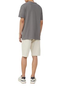 Grijze t-shirt met korte mouwen met een gestructureerde patch op de linkermouw, gecombineerd met lichtgekleurde shorts en sneakers.