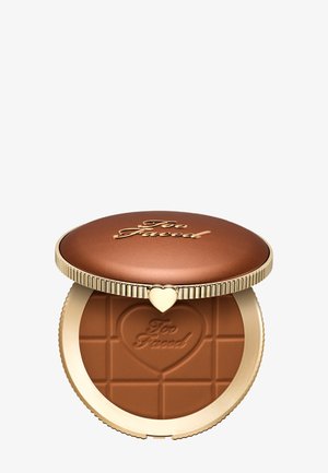 Bronzer compact avec un couvercle bronze portant le logo doré "Too Faced" et un fermoir en forme de cœur, poudre embossée d’un cœur et du nom de la marque.