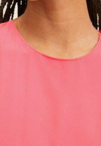 Rosa Bluse aus glattem, weichem Stoff mit rundem Ausschnitt und dezentem Drapée, die ein einfaches und klares Design zeigt.