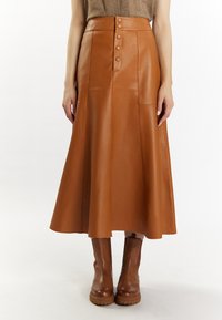 Brown leather maxi skirt with a high waist, five buttons down the front, and a flared silhouette. Worn with matching brown heeled boots.