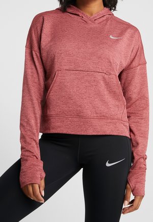 Person wearing a red heathered hoodie with thumb holes and black leggings, both featuring a white Nike swoosh logo.