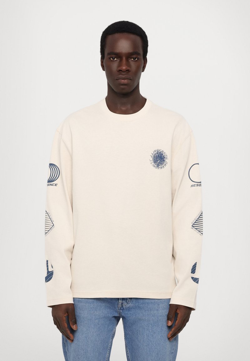 Beige long-sleeve T-shirt in cotton with blue graphic designs on the chest and sleeves, featuring a round neckline and relaxed fit.