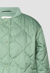 Veste matelassée vert clair avec des motifs de couture ondulés, fermeture à boutons pression, col côtelé et une boucle de suspension à l'intérieur de l'encolure.