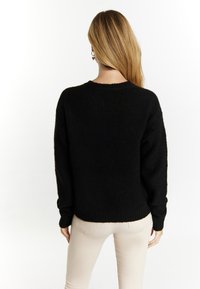 Czarny sweter z dzianiny o luźnym kroju, z rypruszanym dołem i długimi rękawami, wykonany z fakturowanej, miękkiej tkaniny i z dekoltem typu crew neck.