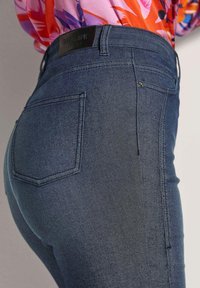 Blauwe denim jeans met een slanke pasvorm, een gemiddelde taillehoogte en twee achterzakken met een leren merkembleem op de tailleband achter.