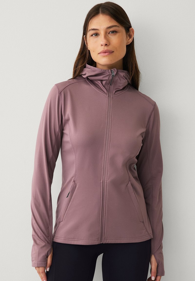Giacca aderente con zip in mauve tenue, realizzata in materiale liscio ed elastico. Presenta maniche lunghe, un colletto alto e tasche laterali.