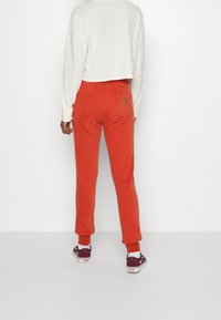 Oranžové tepláky s úzkým kotníkem, s kapsou na zadní straně, v kombinaci s bordovými teniskami. Bílý zkrácený dlouhý rukáv.