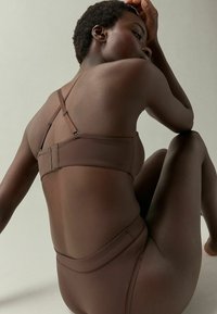 Brūns bikini komplekts ar siksnu dizainu, mīkstu tekstūru, augstu jostasvietu un minimālo šuvju detaļām. Vienkārša, bezšuvju estētika.