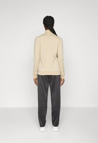 Beige long-sleeve top with a fitted design, paired with dark gray loose pants. Smooth fabric, minimal detailing, and standard cuffs.