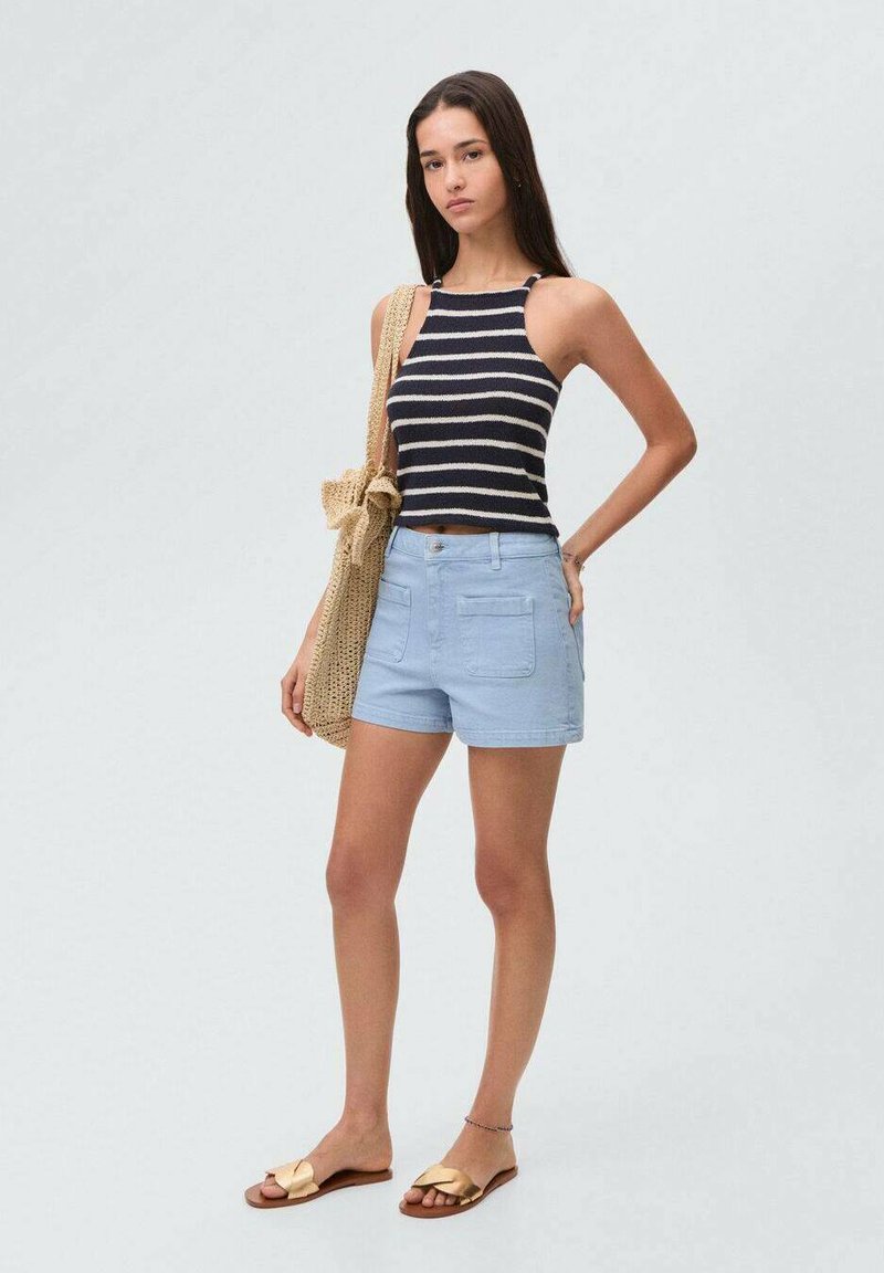 Svetlo modri šortsi s sprednjimi žepe, v kombinaciji z temno modro in belo prugasto brezrokavno majico. Model drži bež pleteno torbo. Zlati sandali dopolnjujejo videz.