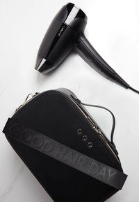 Zwarte ghd flight+ föhn met een zwarte driehoekige draagtas met het label "GOOD HAIR DAY" op een witte achtergrond.