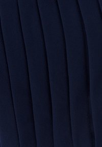 Temno modra tkanina z mehko teksturo, ki ima navpične gube, ki ustvarjajo ritem vzorec po celotnem materialu.