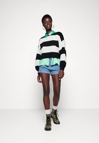 Stripet genser i svart og hvitt, lagdelt over en lys grønn skjorte, paret med denimshorts og blomstrete combat boots.