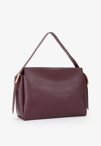 Bordeaux læder håndtaske med en blød tekstur, en struktureret form og et enkelt top-håndtag. Udstyret med hardware akcenter i guld-tone.