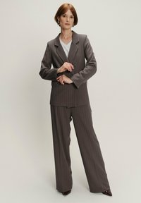 Chaqueta de traje gris a rayas con solapas en pico, cierre de un solo botón, combinada con pantalones grises holgados, llevada sobre una camiseta blanca.