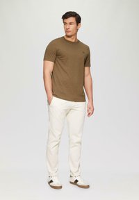 T-shirt vert olive à manches courtes avec un col rond, associé à un pantalon blanc et des baskets claires avec des accents marron.