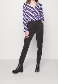 Multicolored striped blouse in purple, blue, and white with a V-neck; paired with fitted black trousers and chunky black heeled boots.