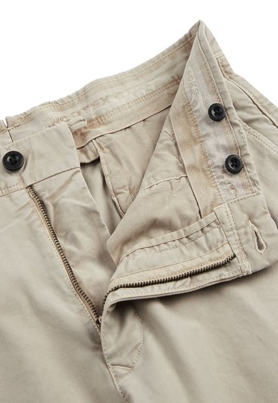 Pantalones de algodón beige con cremallera, dos botones negros y una textura suave. Presenta costuras cosidas y bucles internos en la cintura.