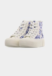 Υψηλά πάνινα αθλητικά παπούτσια με λευκές σόλες και μπλε λουλουδάτα μοτίβα σε κρεμ ύφασμα, δεμένα με κορδόνια και τοποθετημένα δίπλα το ένα στο άλλο σε απλό φόντο.